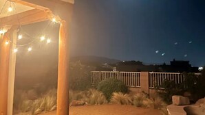 Un espace extérieur aménagé en terrasse, agrémenté de guirlandes lumineuses, d’une pergola en bois et offrant une vue sur les collines lointaines.