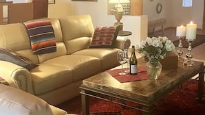 Un salon chaleureux avec un canapé en cuir, une table basse sur laquelle se trouvent une bouteille et des fleurs, et deux bougies allumées.