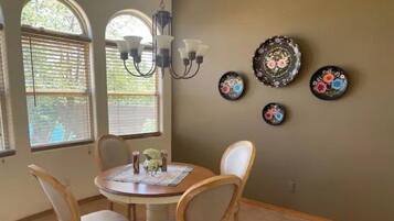 A dining area with a round table, four chairs, a chandelier, and decorative plates on the wall.