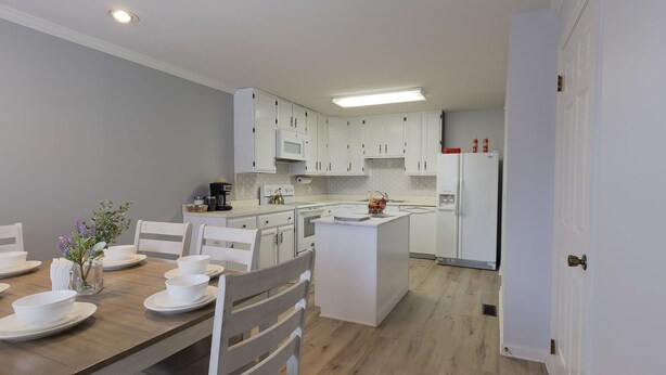 A modern kitchen with white cabinets, a central island, and a dining area with a wooden table and chairs. - Charming Lafayette Condo: Cozy Retreat in Indiana (Lafayette)