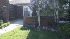 A residential house with a brick exterior, a front porch, and a small garden area with a tree bearing purple flowers. - Charming Lafayette Condo: Cozy Retreat in Indiana (Lafayette)