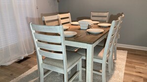A dining table set with plates, cutlery, and a candle. There are four chairs around the table, and a plant hangs on the wall. - Charming Lafayette Condo: Cozy Retreat in Indiana (Lafayette)