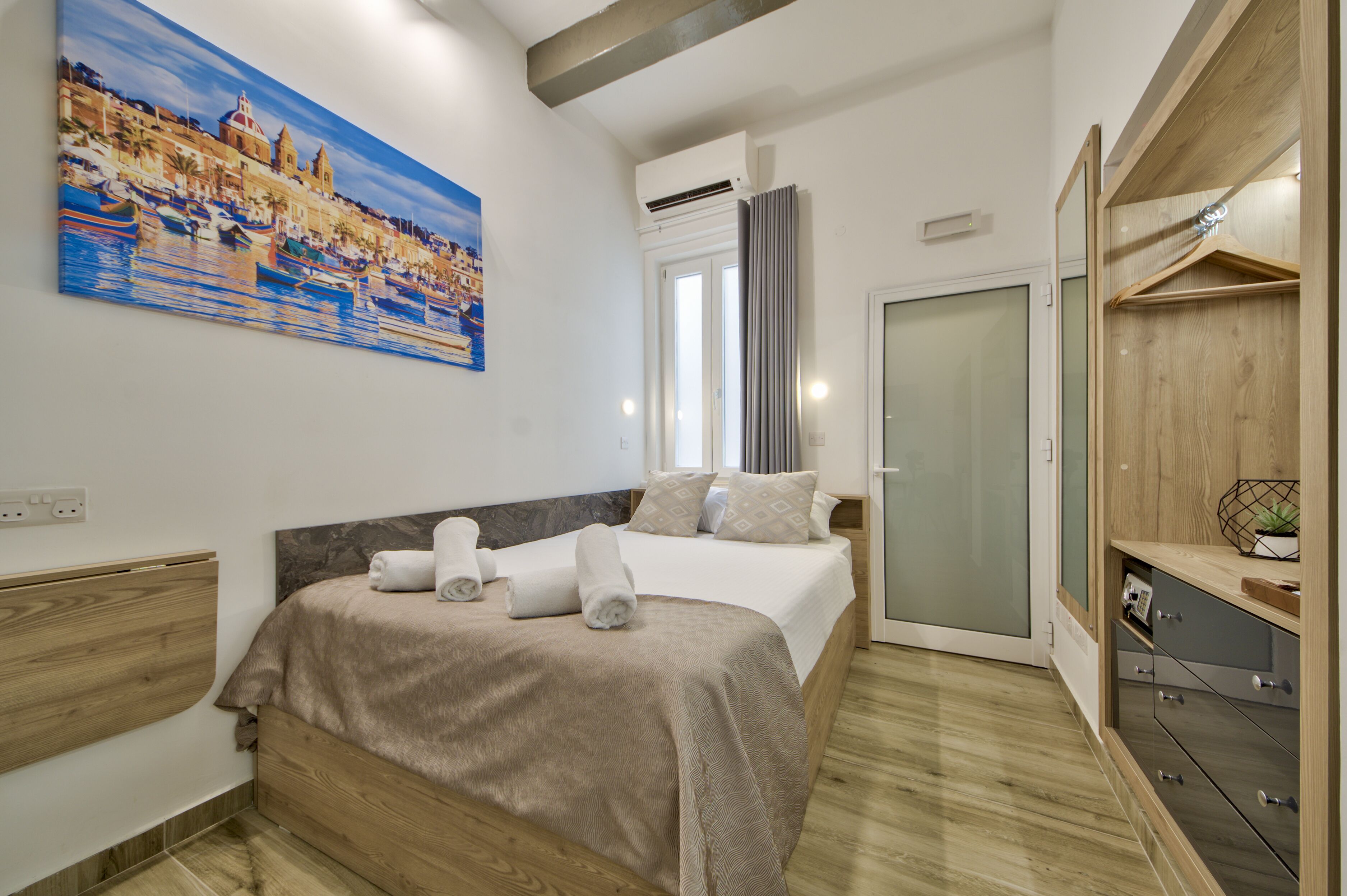 Una habitación de hotel moderna con cama, un cuadro, un armario y un escritorio pequeño.