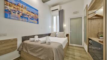 Una habitación de hotel moderna con cama, un cuadro, un armario y un escritorio pequeño.