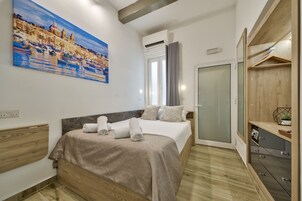 Una habitación de hotel moderna con cama, un cuadro, un armario y un escritorio pequeño.