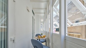 Een smalle gang met een tafel, stoelen, een kleine plant en een raam met uitzicht op gebouwen.