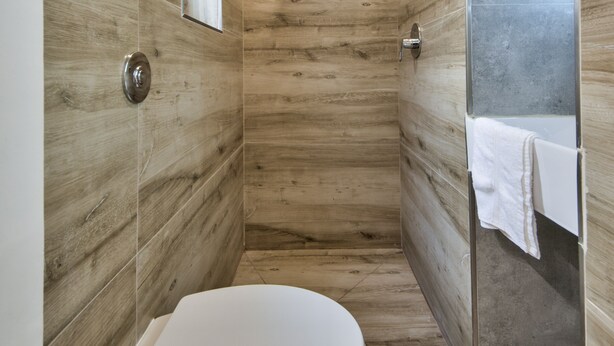 Een moderne badkamer met een houten wandbekleding, een wit toilet en een douchecabine met glazen wanden.