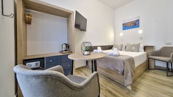 Een moderne hotelkamer met een bed, twee fauteuils, een klein tafeltje met een plant, een aan de muur bevestigde televisie en een schilderij.