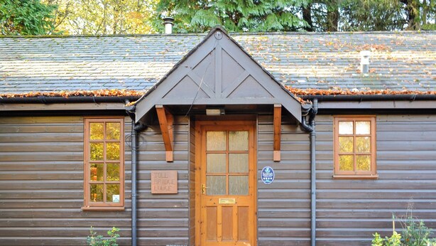 Une petite maison en bois dotée d’une porte centrale en bois, de deux fenêtres de chaque côté et d’une enseigne indiquant qu’il s’agit du poste de péage d’un pont.