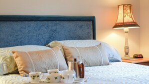 Un lit bien fait, avec un plateau contenant du thé, des coussins et une lampe sur une table de chevet.