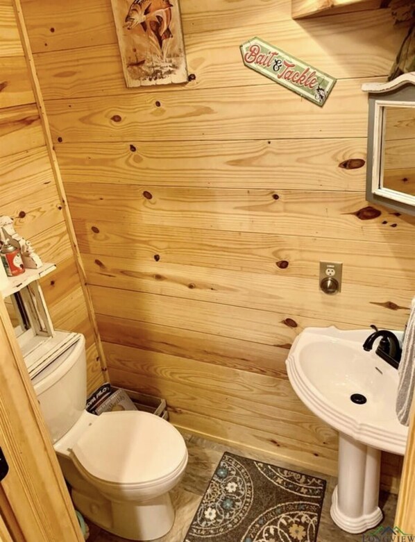 Een kleine houten badkamer met toilet, wastafel en een 'Bait & Tackle' bord aan de muur.