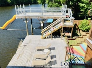 A wooden dock with a small bridge, a slide, and a seating area with a table and chairs.