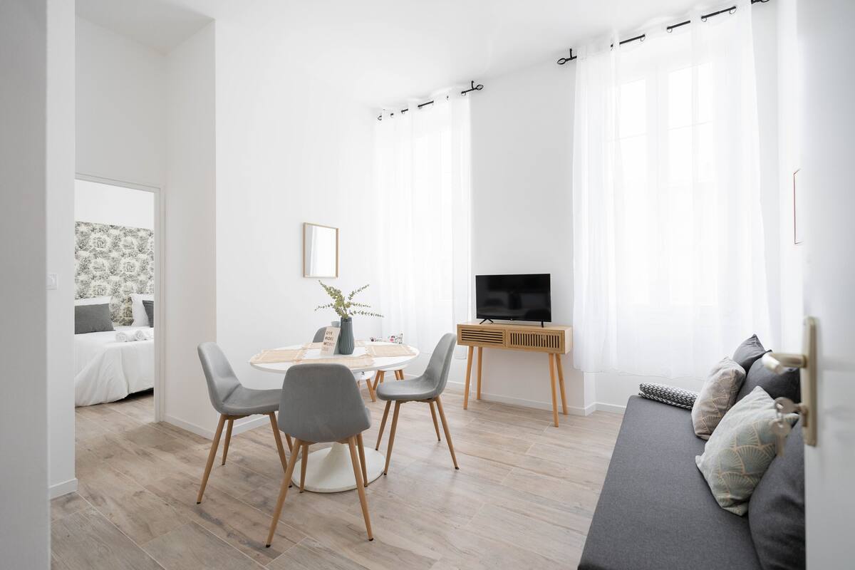 Una sala de estar moderna con comedor, un televisor sobre un mueble de madera y un sofá con cojines.