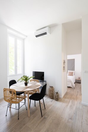 Una habitación moderna y bien iluminada con comedor, televisor y cama con cabecera estampada.