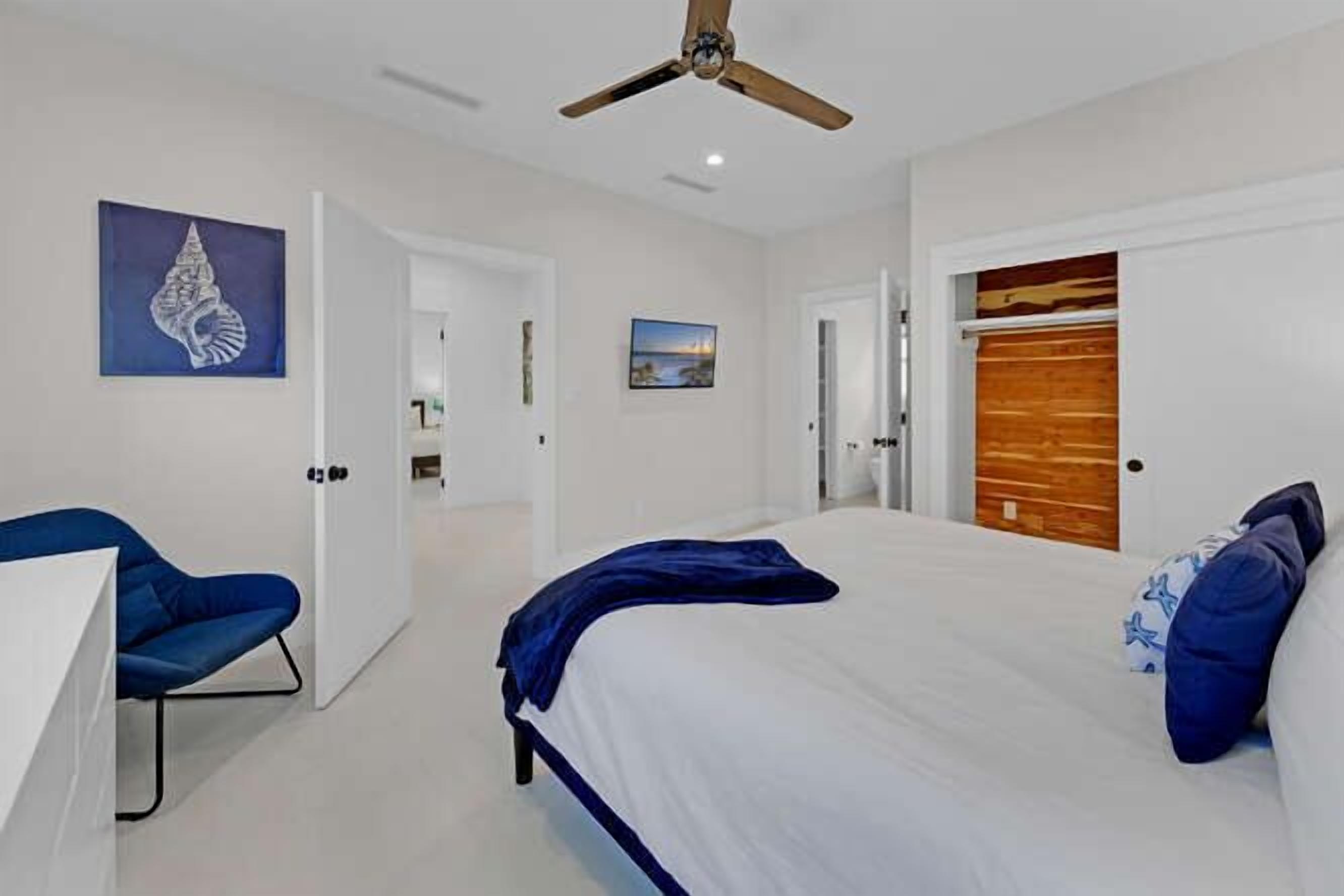 A bedroom with a bed, a ceiling fan, a blue chair, and a wooden door.