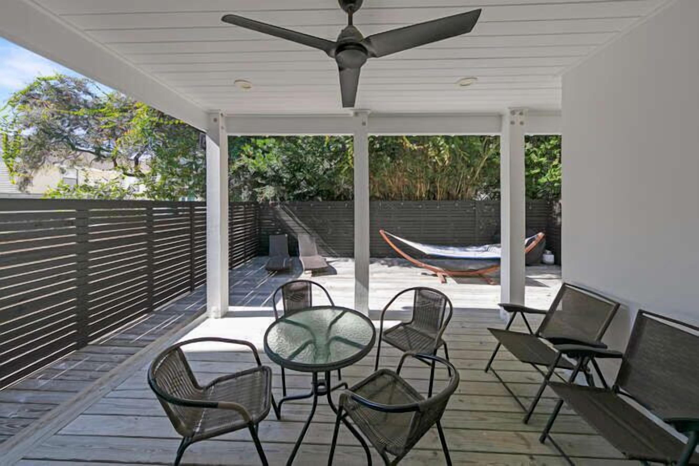 A covered patio with a ceiling fan, outdoor seating, and a hammock.