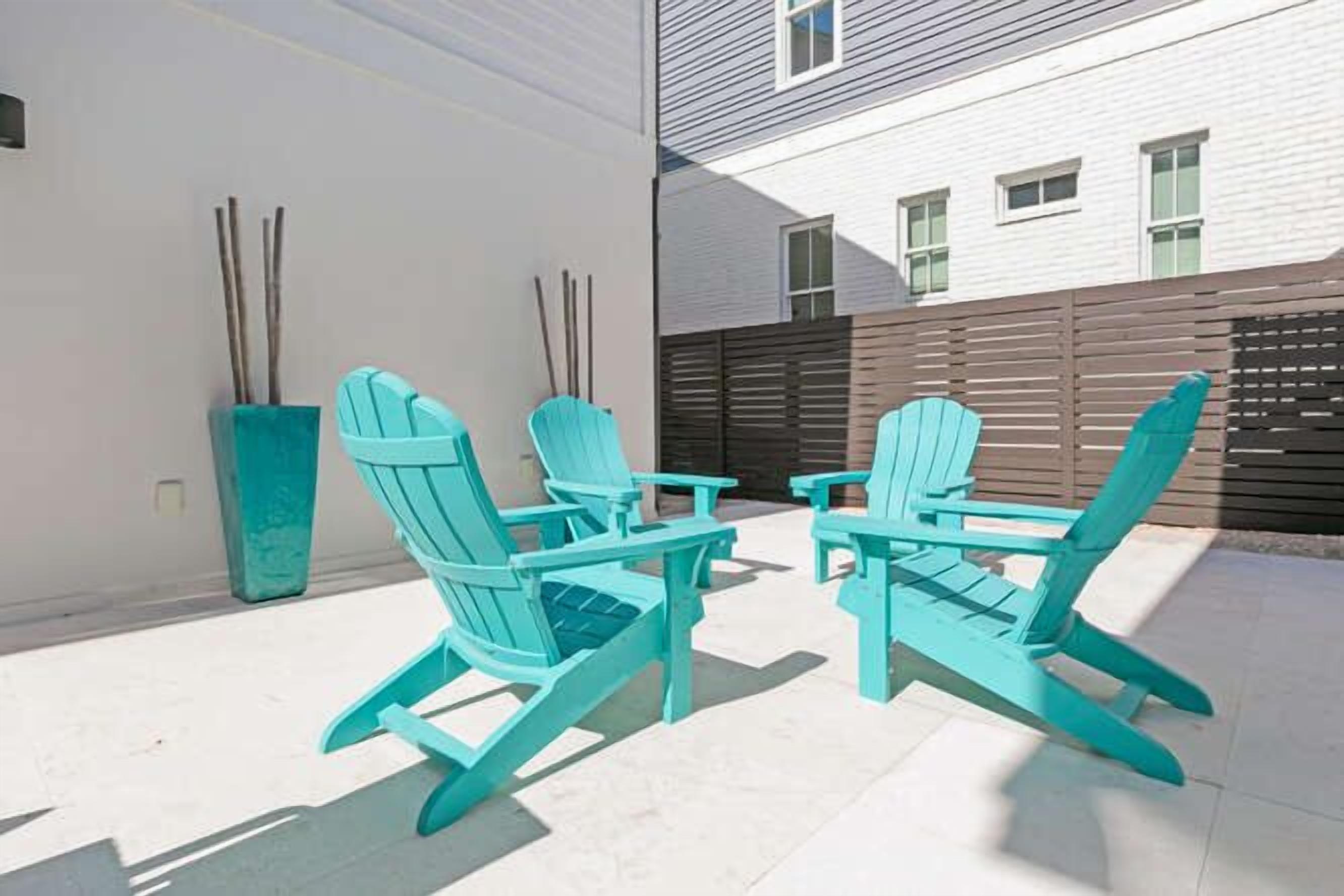 Une terrasse avec deux fauteuils Adirondack turquoise et une petite table, un mur blanc et une clôture en bois.