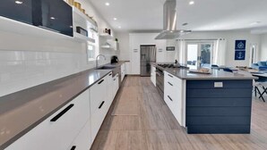 A modern kitchen with white cabinets, a central island, and a stainless steel range hood. - Old Seagrove "Thyme by the Sea" |3BR| 2 Kings| Sleeps 9| 250ft from Beach! (Santa Rosa Beach)