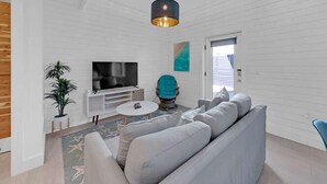 Ein modernes Wohnzimmer mit einem grauen Sofa, einem Fernseher, einem blauen Sessel und einem kleinen Tisch.