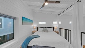 Ein Schlafzimmer mit einem großen Bett, einem Deckenventilator, einem Fenster und einem Nachttisch mit einer Lampe.