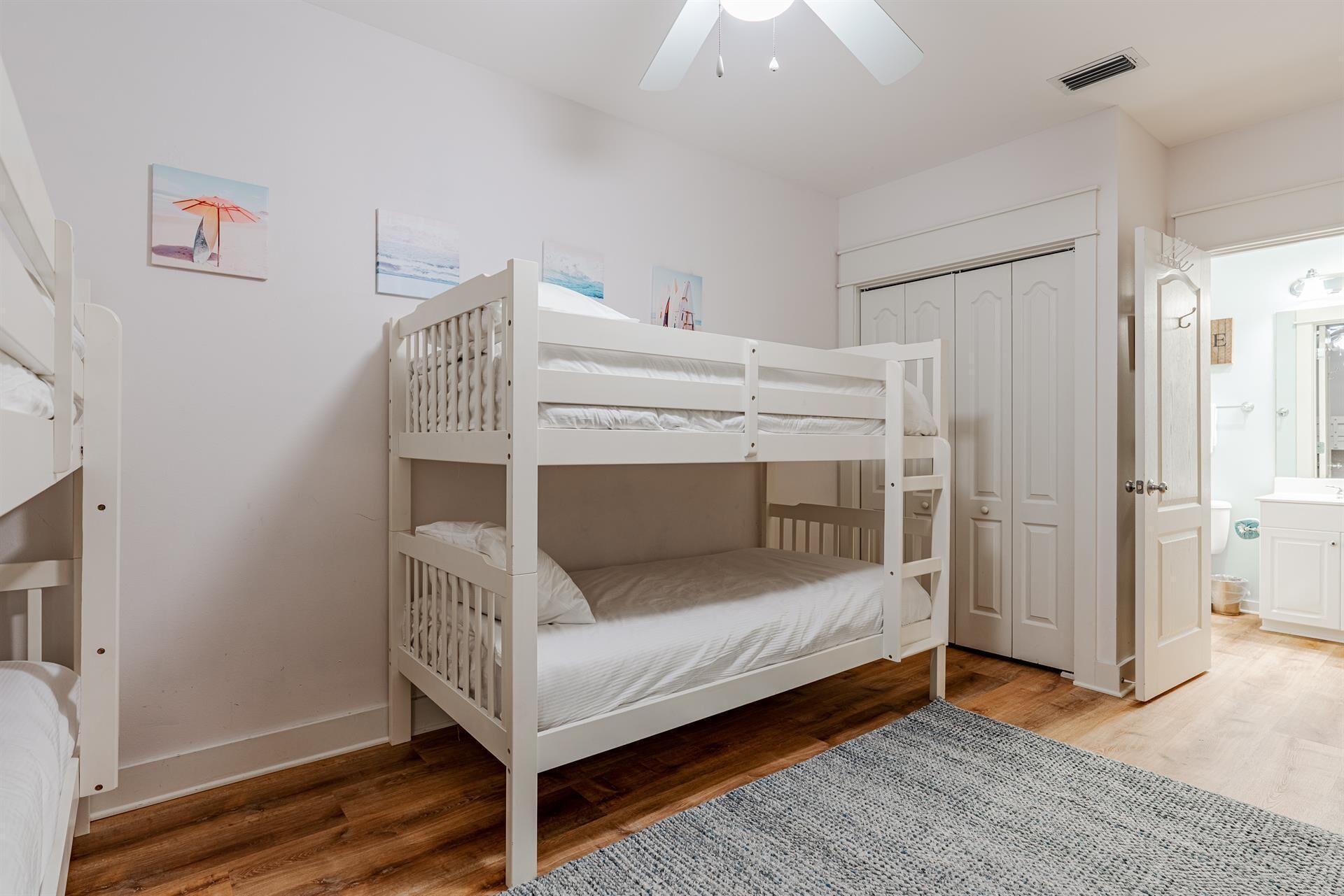 Une chambre avec des lits superposés, des murs blancs, un plancher en bois et une porte donnant sur une salle de bain.