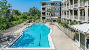 A swimming pool with a diving board, surrounded by a fence and lounge chairs.