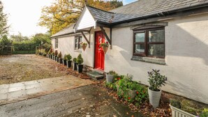 Une maison blanche avec une porte rouge, un petit porche et des plantes en pot.