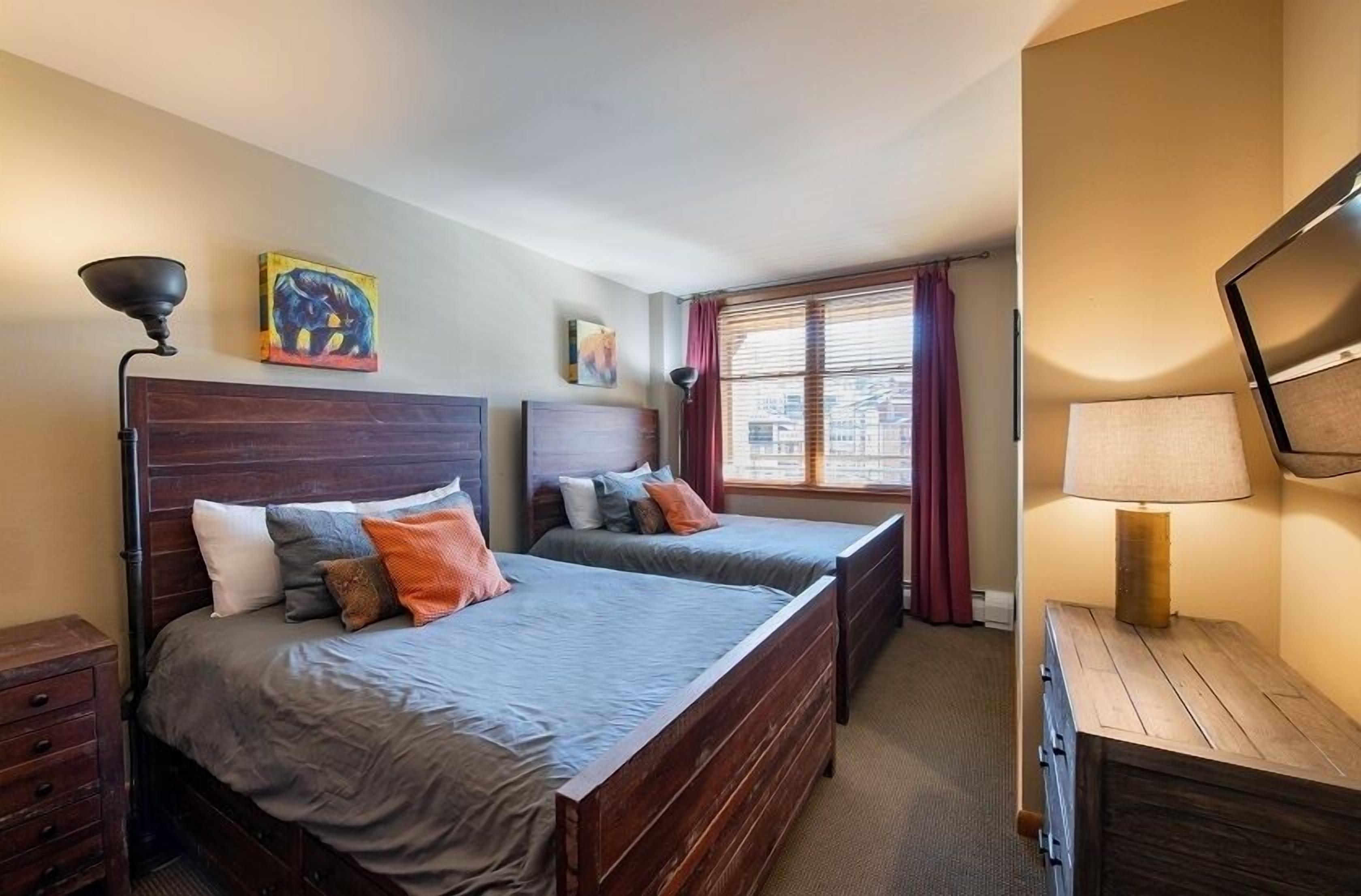 A bedroom with two wooden beds, a nightstand, a lamp, and a painting on the wall.