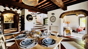 A dining area with a wooden table set for four, a staircase, and a view of a bedroom with a bed and a window.