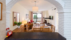 Un coin repas avec une table noire, des chaises en bois, une plante en pot et un canapé avec des coussins rouges.