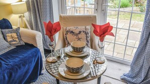 A dining area with a table set for two, featuring patterned tableware and a view through a glass door.