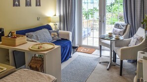 A compact living space with a sofa, a small table, a chair, and a view through a glass door.