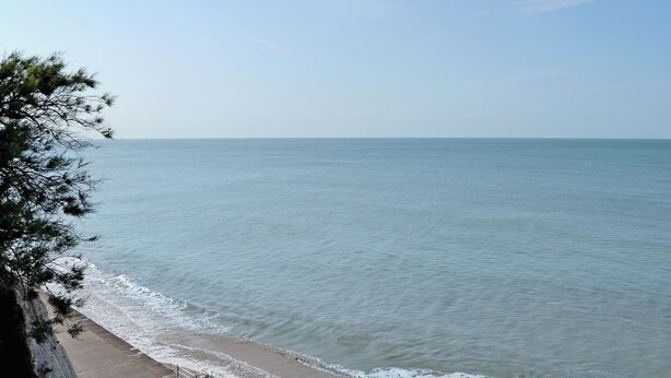A coastal walkway with a railing, leading to the sea.