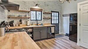Une cuisine moderne avec un mur de briques en guise de crédence, des plans de travail en bois, une cuisinière encastrée et un réfrigérateur en acier inoxydable.