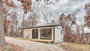 Une cabane moderne dotée d’une grande porte-fenêtre coulissante, d’un petit porche et d’une allée en gravier bordée d’arbres.
