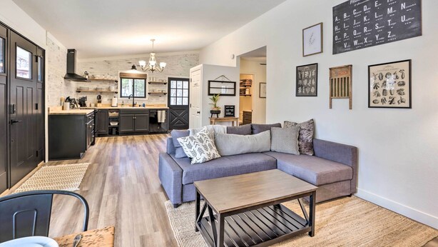 Un salon moderne avec un canapé gris, une table basse en bois et une cuisine en arrière-plan.