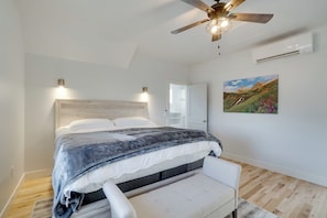 Ein Schlafzimmer mit Bett, Nachttischen, Deckenventilator, Klimaanlage und Landschaftsbild an der Wand.