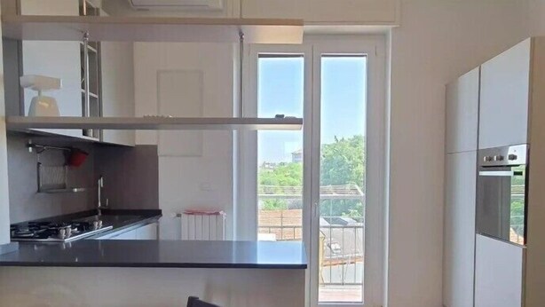 A modern kitchen with a black countertop, stainless steel appliances, and a sliding glass door leading to a balcony.
