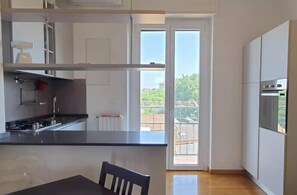 A modern kitchen with a black countertop, stainless steel appliances, and a sliding glass door leading to a balcony. - Titti's Corner (Milan)