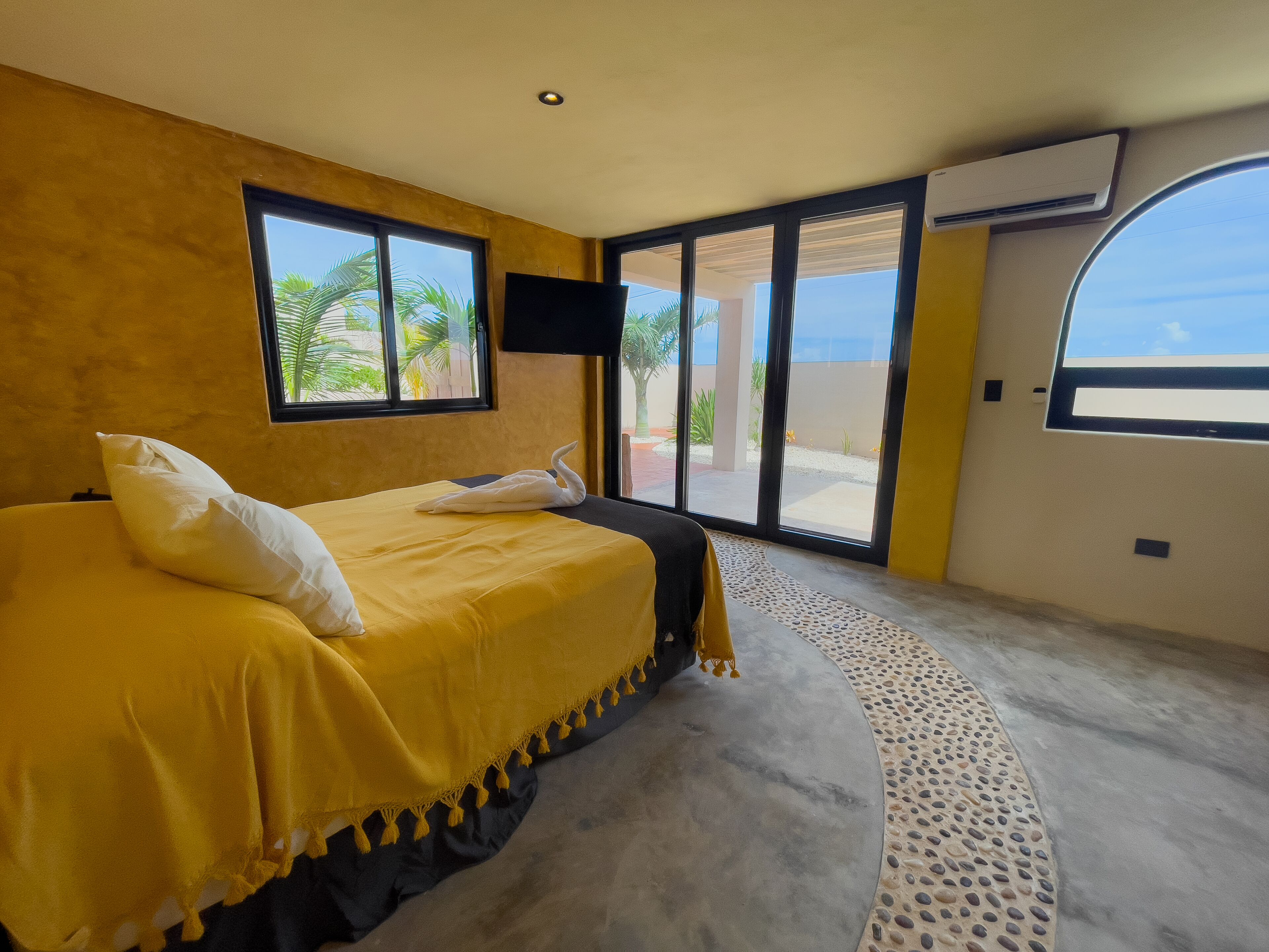A bedroom with a bed, a television, a window, and an air conditioning unit.