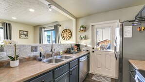 A modern kitchen with a large island, stainless steel appliances, and a view of the city through the window. - Updated Townhome: Near Airport & Shopping! (Anchorage)