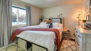 A bedroom with a bed, bedside table, dresser, and a window with curtains. - Updated Townhome: Near Airport & Shopping! (Anchorage)