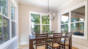 Une salle à manger avec une table et des chaises en bois, de grandes fenêtres et un lustre.