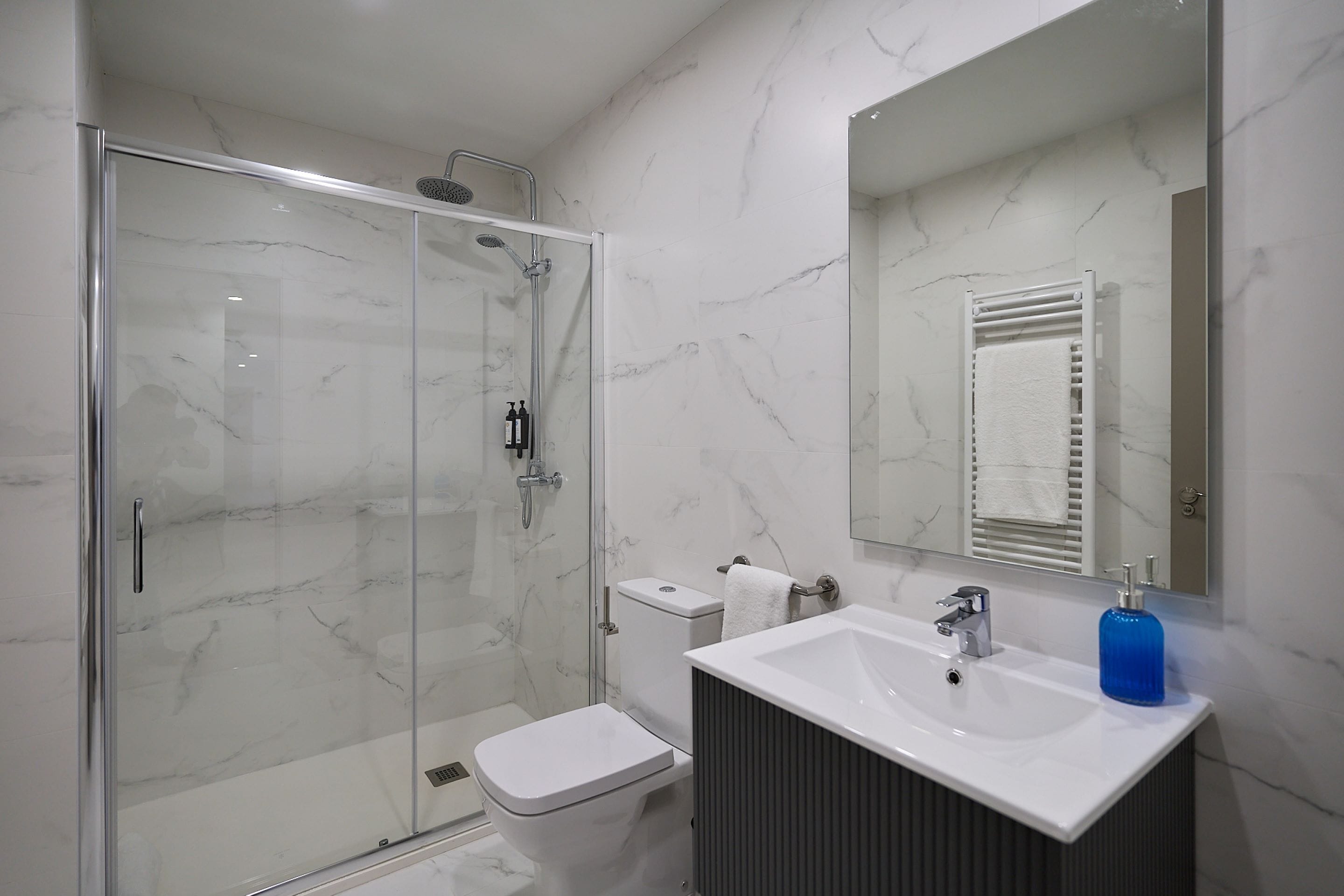 Un baño moderno con ducha de vidrio, lavamanos blanco y un espejo grande.