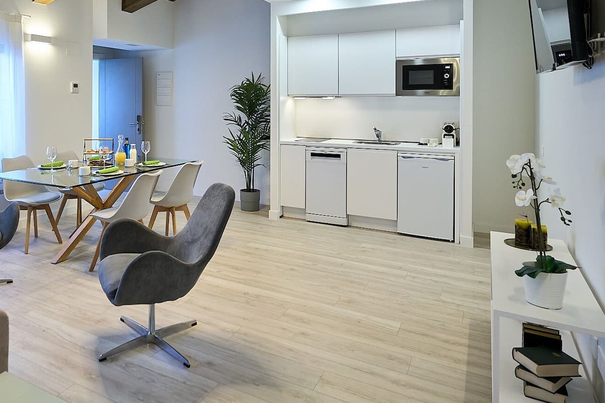 A modern living room with a glass dining table, grey chairs, a sofa, and a potted plant.