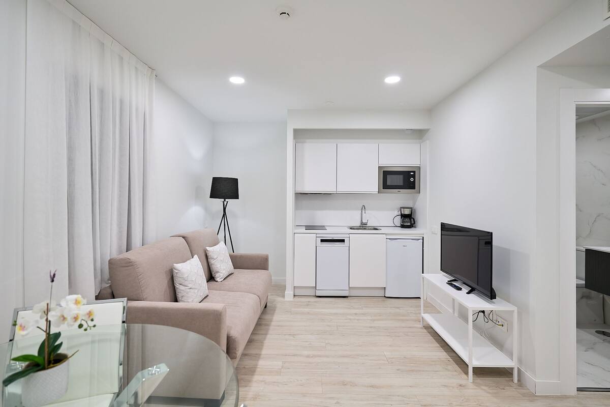 A modern apartment with a living room, kitchenette, and a TV on a stand.