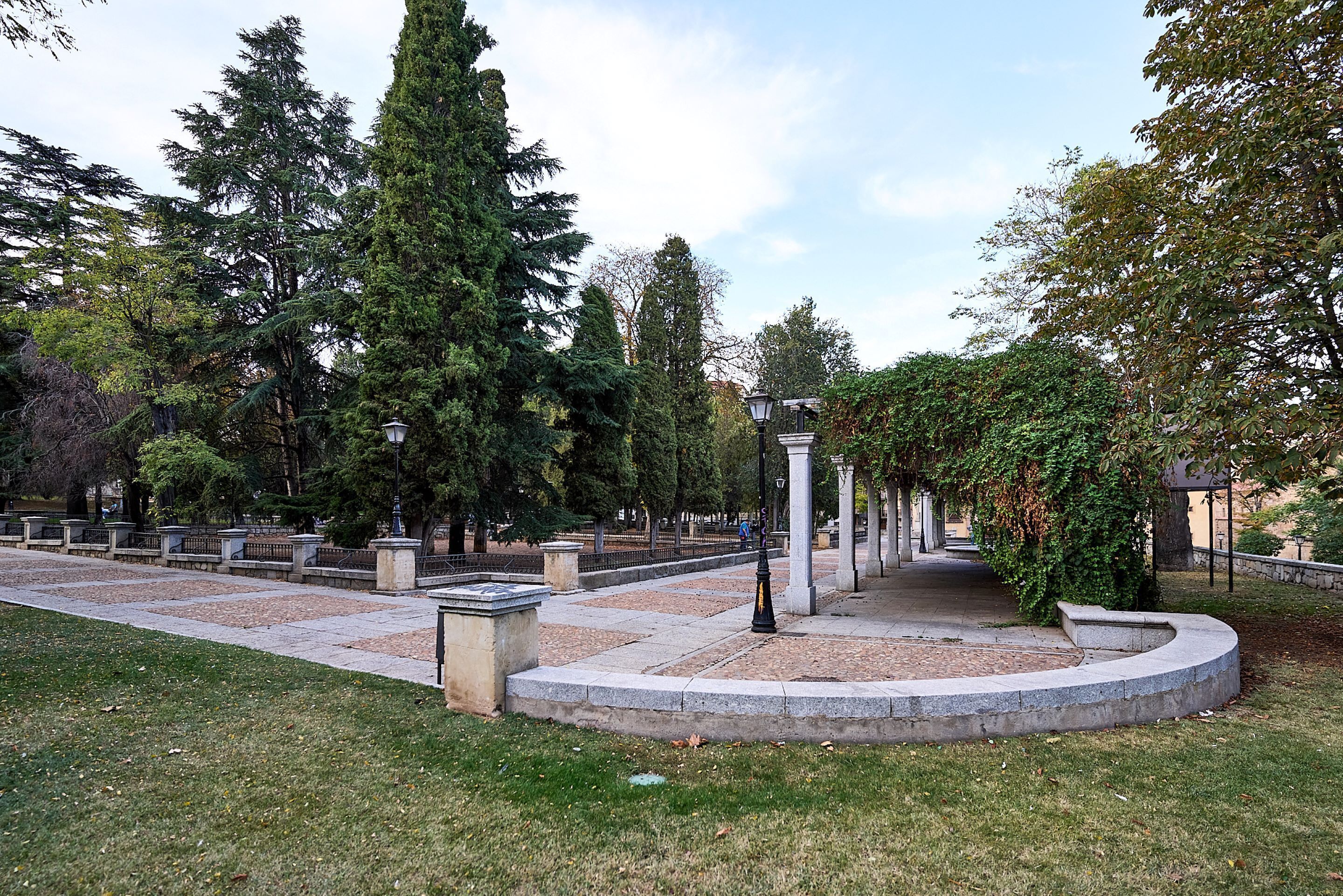 Um parque com um banco de pedra circular, postes de luz e árvores altas.