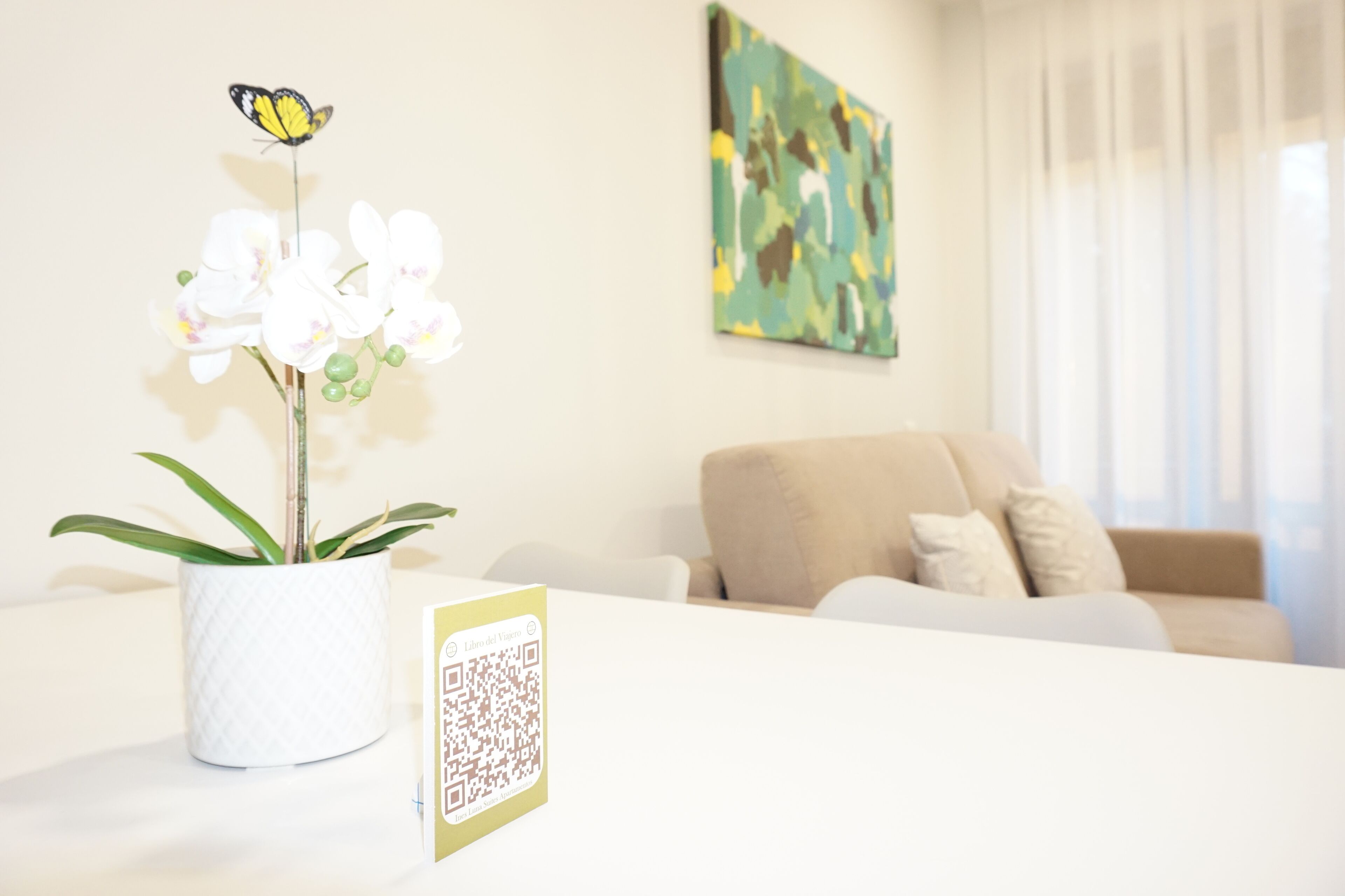 A living room with a white sofa, a white vase with white orchids, and a QR code on a table.