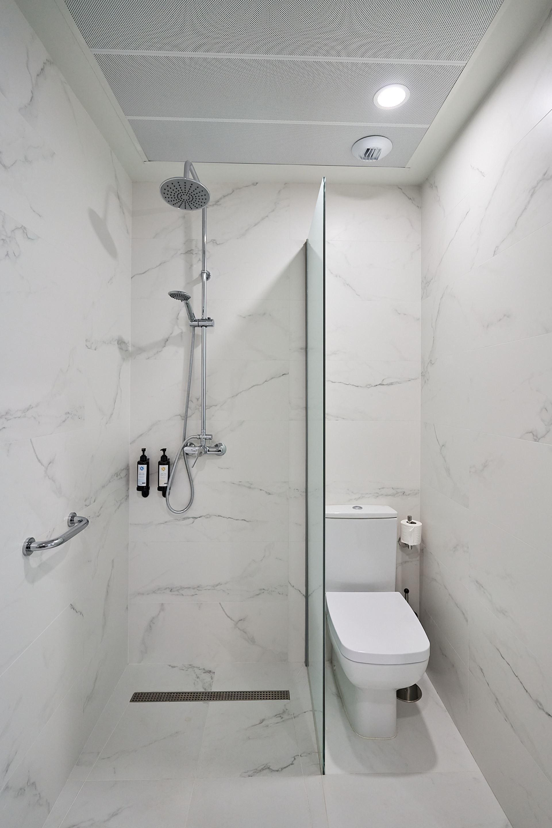 A modern bathroom with a shower, toilet, and marble walls.