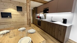 Una cucina moderna con mobili in legno, un piano di lavoro bianco e una zona pranzo con un tavolo in legno apparecchiato per quattro persone.